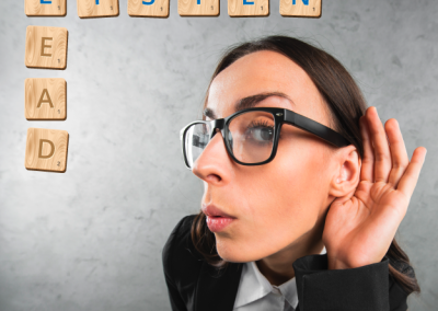 Businesswoman with glasses holding hand to ear as if listening, with Scrabble-style letters in the background.